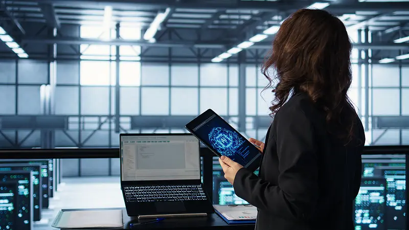 A professional analyzing system data on a tablet and laptop inside a modern server facility, representing ServiceNow ITOM Implementation and real-time operational monitoring.