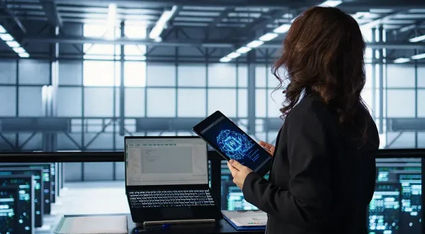 A professional analyzing system data on a tablet and laptop inside a modern server facility, representing ServiceNow ITOM Implementation and real-time operational monitoring.