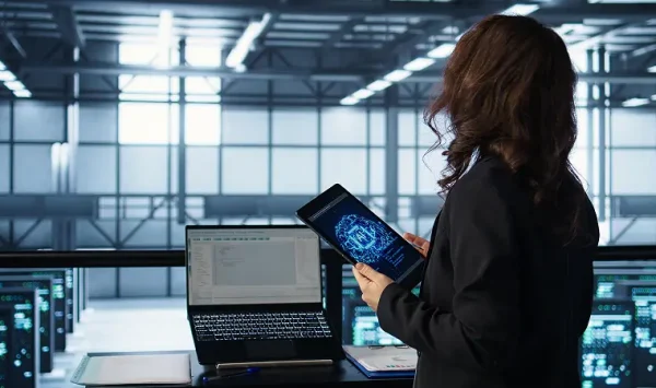 A professional analyzing system data on a tablet and laptop inside a modern server facility, representing ServiceNow ITOM Implementation and real-time operational monitoring.